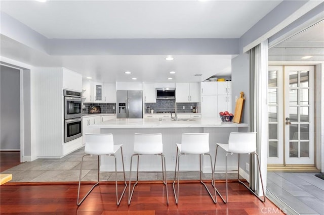 kitchen with kitchen peninsula, a kitchen bar, sink, white cabinetry, and appliances with stainless steel finishes