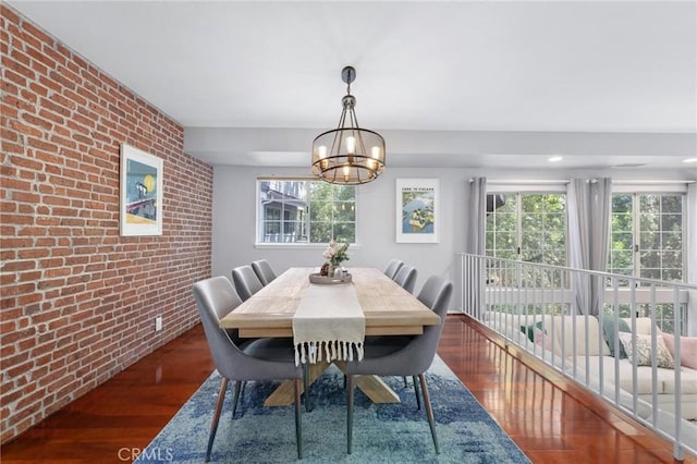 dining area with dark wood-type flooring, brick wall, and a notable chandelier