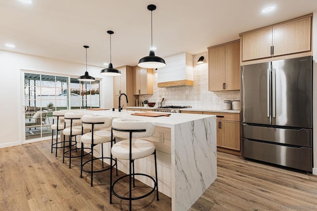 kitchen featuring light brown cabinetry, stainless steel fridge, and an island with sink