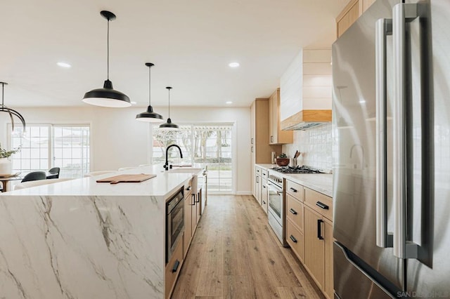 kitchen with light brown cabinetry, stainless steel appliances, and pendant lighting