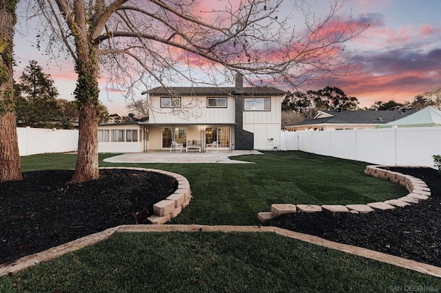 back house at dusk featuring a yard and a patio