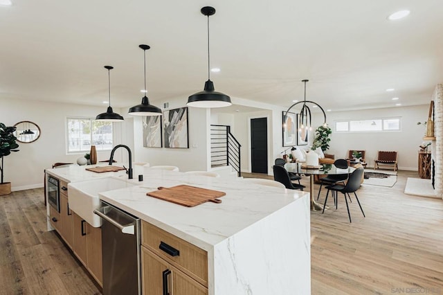 kitchen featuring a large island, decorative light fixtures, stainless steel dishwasher, light stone counters, and sink