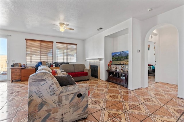 living room featuring ceiling fan, a fireplace, a textured ceiling, and light tile patterned flooring