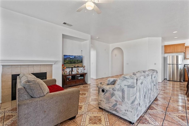 tiled living room featuring ceiling fan and a tiled fireplace