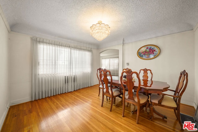 dining area featuring an inviting chandelier, crown molding, wood-type flooring, and a textured ceiling