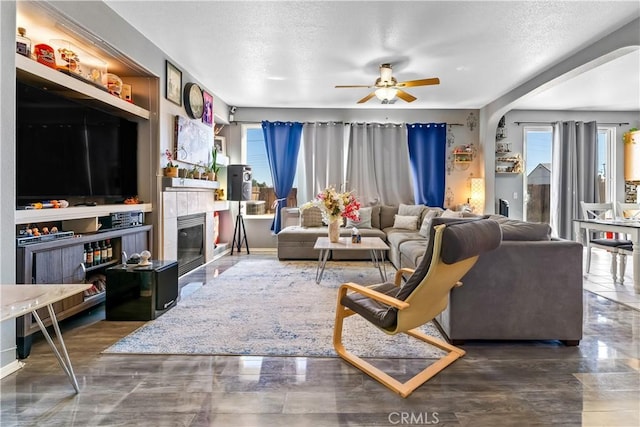 living room featuring a textured ceiling, ceiling fan, and a tile fireplace