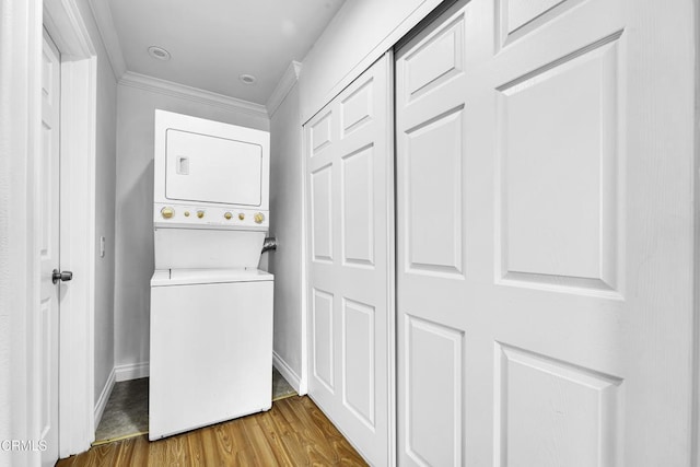 clothes washing area with stacked washer and clothes dryer, ornamental molding, and hardwood / wood-style flooring