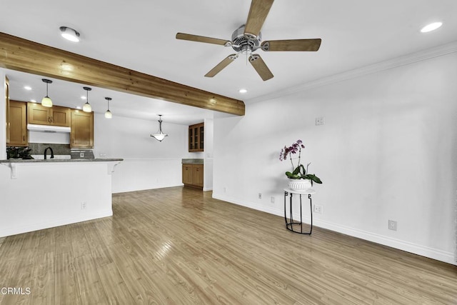 unfurnished living room featuring ceiling fan, wood-type flooring, ornamental molding, and beamed ceiling