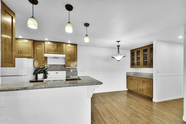 kitchen featuring white appliances, decorative light fixtures, dark stone countertops, light hardwood / wood-style floors, and a breakfast bar area