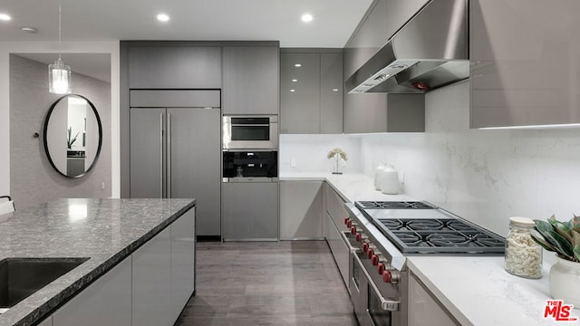 kitchen featuring ventilation hood, hanging light fixtures, high quality appliances, gray cabinets, and dark stone counters