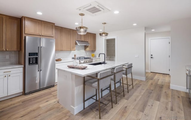 kitchen with an island with sink, sink, hanging light fixtures, backsplash, and high end refrigerator