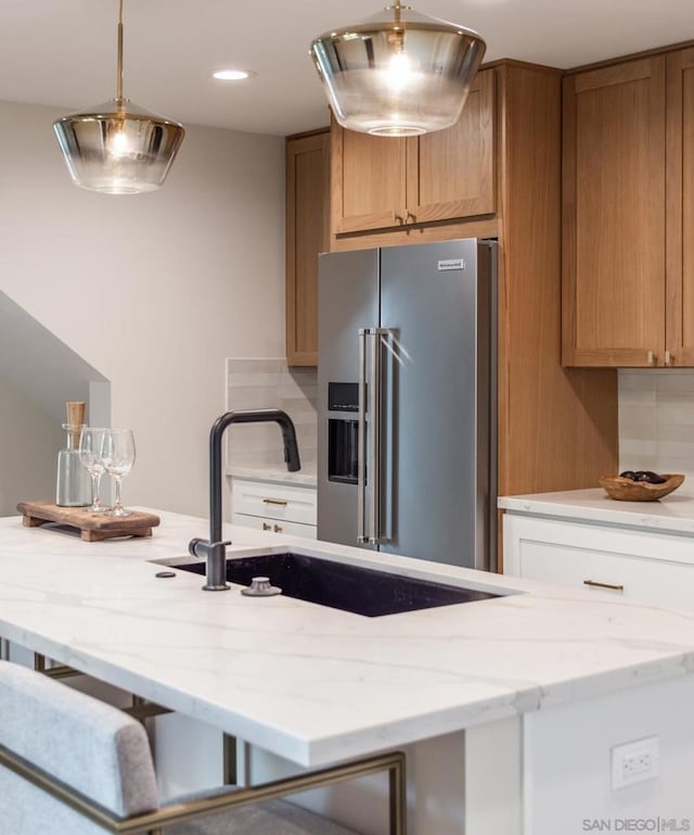 kitchen featuring light stone countertops, white cabinets, sink, hanging light fixtures, and high end fridge