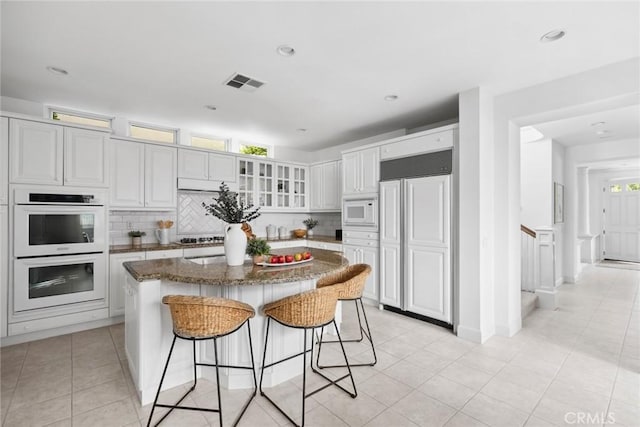 kitchen with tasteful backsplash, white cabinetry, a kitchen bar, a center island, and built in appliances