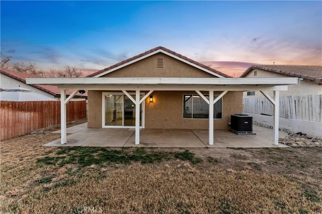 back house at dusk with a patio, a lawn, and central AC