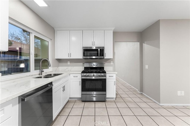 kitchen featuring white cabinets, appliances with stainless steel finishes, sink, light tile patterned flooring, and light stone counters