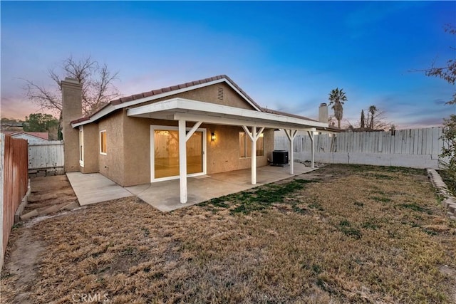 back house at dusk featuring central air condition unit, a lawn, and a patio