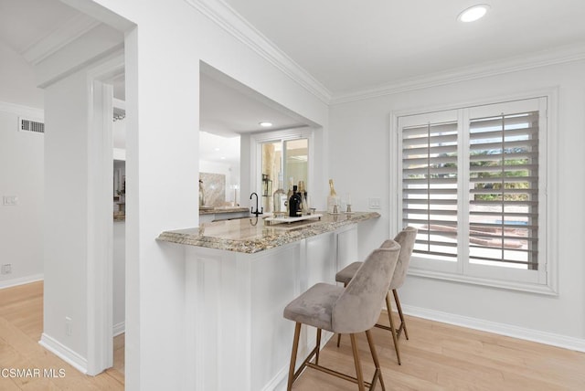 kitchen featuring kitchen peninsula, crown molding, light wood-type flooring, light stone counters, and a breakfast bar