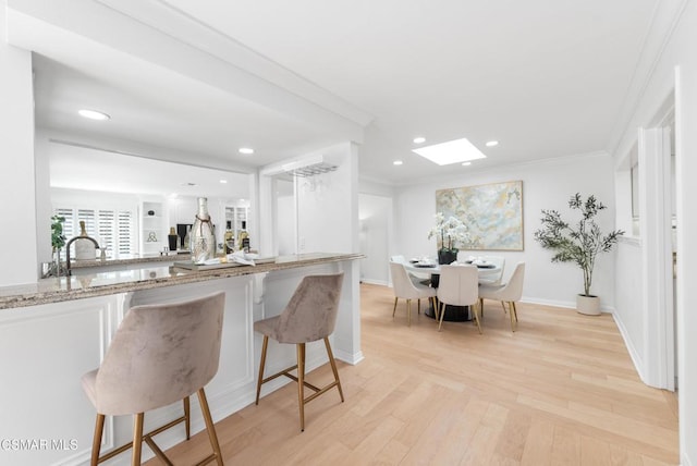 kitchen featuring light stone countertops, a breakfast bar, white cabinets, and a skylight