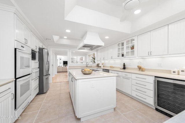 kitchen with premium range hood, a raised ceiling, white cabinets, and beverage cooler