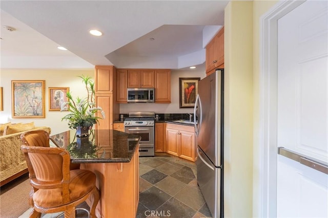 kitchen featuring sink, a breakfast bar area, dark stone countertops, appliances with stainless steel finishes, and a tray ceiling