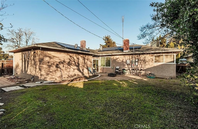 back of property with a patio area, a lawn, and solar panels