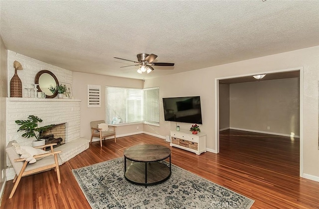 living room featuring ceiling fan, hardwood / wood-style floors, a brick fireplace, and a textured ceiling