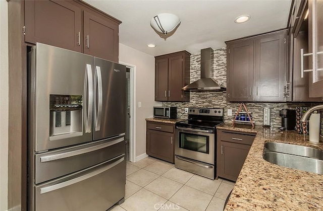 kitchen featuring appliances with stainless steel finishes, backsplash, wall chimney range hood, light stone counters, and sink