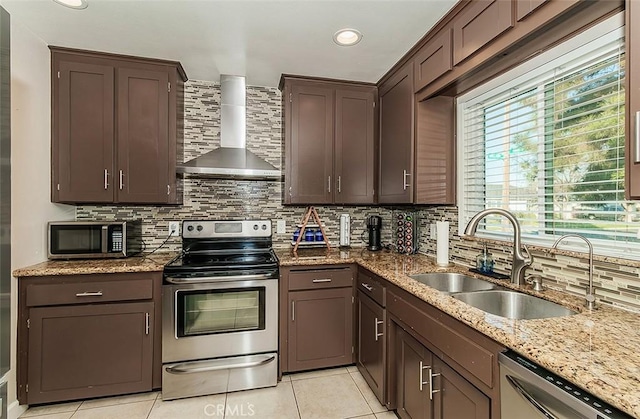 kitchen featuring wall chimney range hood, stainless steel appliances, sink, backsplash, and light tile patterned flooring