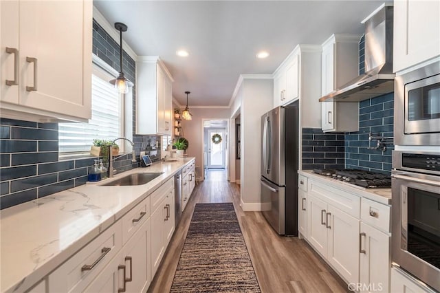 kitchen with sink, hanging light fixtures, stainless steel appliances, white cabinets, and wall chimney exhaust hood