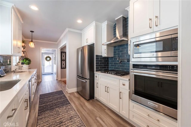 kitchen with appliances with stainless steel finishes, tasteful backsplash, decorative light fixtures, wall chimney range hood, and white cabinets