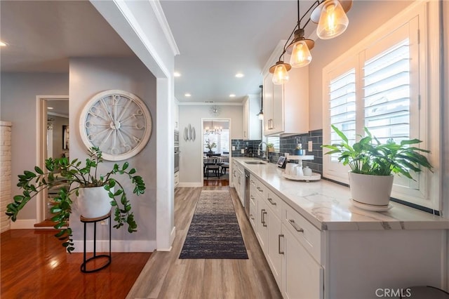 kitchen featuring hardwood / wood-style floors, white cabinets, decorative light fixtures, sink, and light stone counters