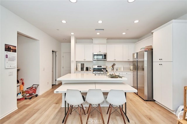 kitchen with white cabinets, a kitchen bar, stainless steel appliances, light hardwood / wood-style floors, and a kitchen island with sink