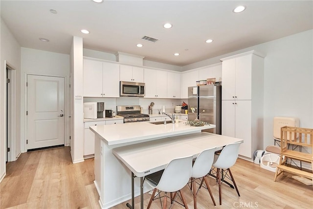 kitchen featuring appliances with stainless steel finishes, white cabinets, a breakfast bar, and an island with sink