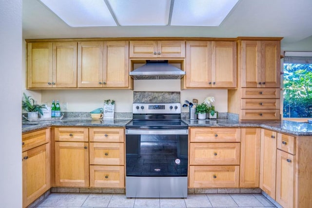 kitchen with light tile patterned floors, wall chimney exhaust hood, dark stone counters, and stainless steel electric stove