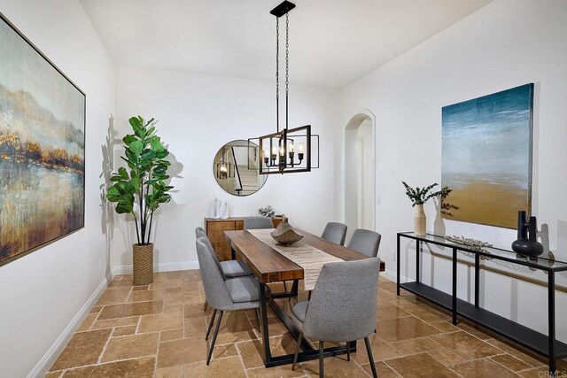 dining space with arched walkways, baseboards, stone tile floors, and an inviting chandelier