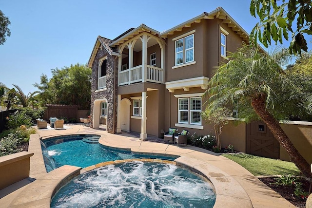 rear view of property featuring stucco siding, stone siding, fence, and an in ground hot tub