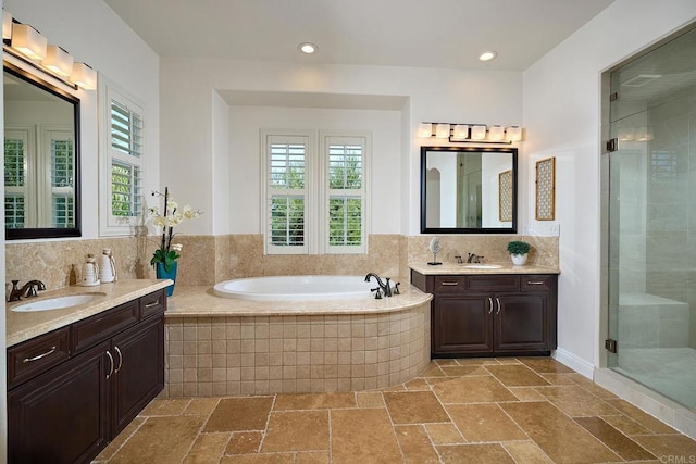 full bathroom featuring stone tile flooring, a stall shower, two vanities, and a sink