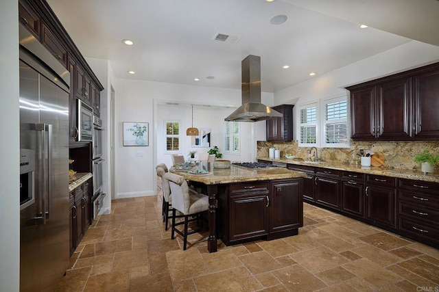 kitchen featuring dark brown cabinetry, stone tile floors, island range hood, stainless steel appliances, and a kitchen island