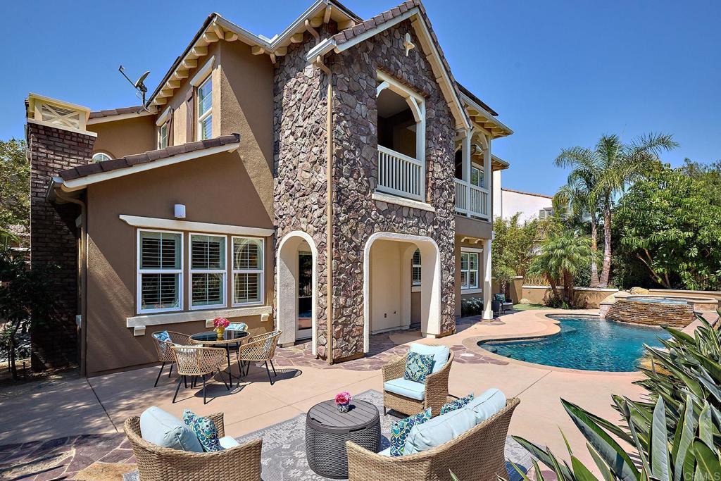 rear view of house with stone siding, a patio, a pool with connected hot tub, and stucco siding