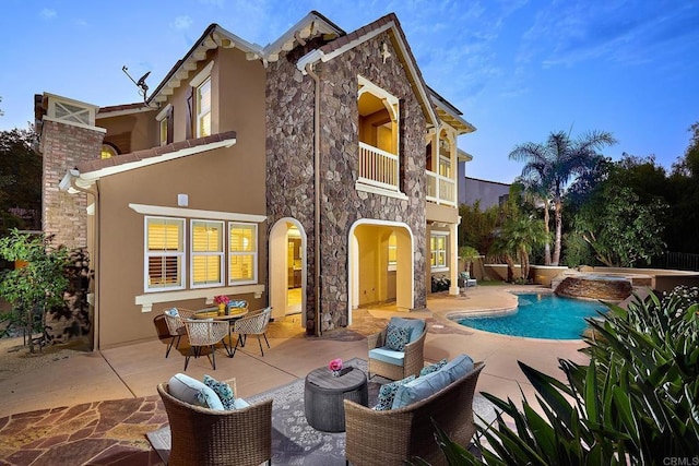 rear view of house featuring a balcony, stone siding, a patio area, and stucco siding