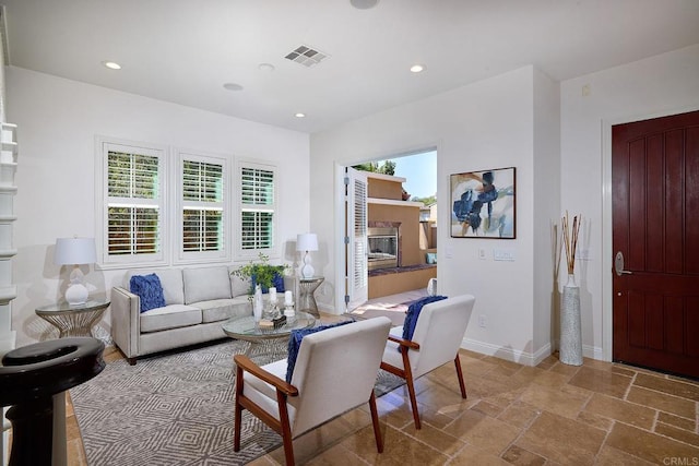 living area featuring stone tile flooring, plenty of natural light, visible vents, and baseboards