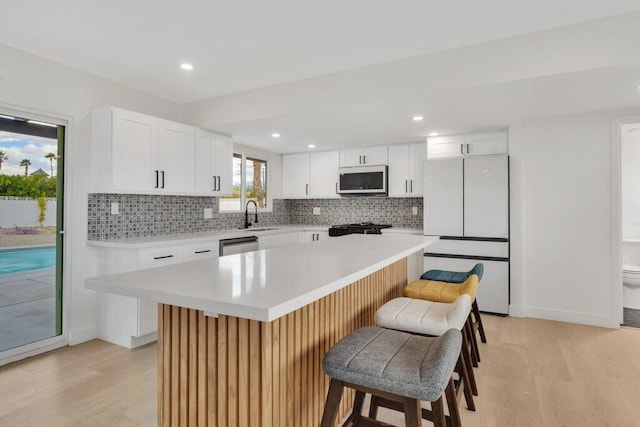 kitchen with white appliances, white cabinets, light hardwood / wood-style flooring, and a kitchen island