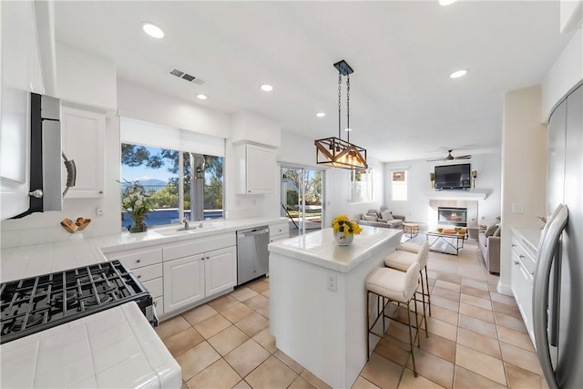 kitchen featuring dishwasher, a kitchen island, white cabinetry, gas range oven, and light tile patterned floors