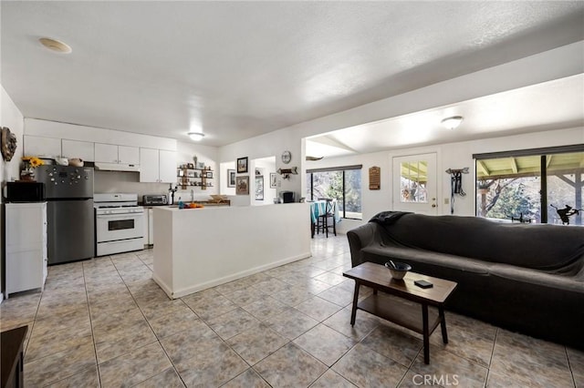 kitchen with white cabinets, white range with gas stovetop, light tile patterned flooring, and stainless steel refrigerator