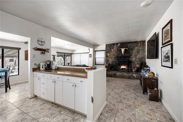 kitchen with white cabinets, kitchen peninsula, a fireplace, and a healthy amount of sunlight