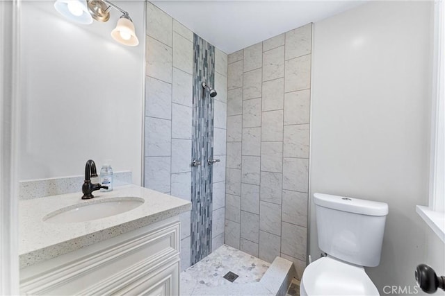 bathroom featuring toilet, tiled shower, and vanity