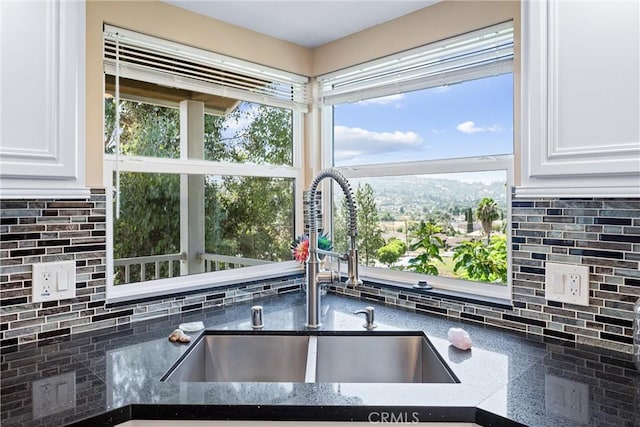 room details with sink, backsplash, white cabinets, and dark stone counters