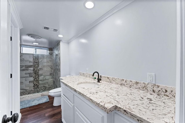 bathroom with toilet, crown molding, a tile shower, and vanity