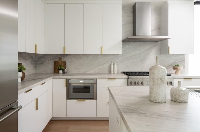 kitchen with white cabinets, appliances with stainless steel finishes, wall chimney exhaust hood, and decorative backsplash