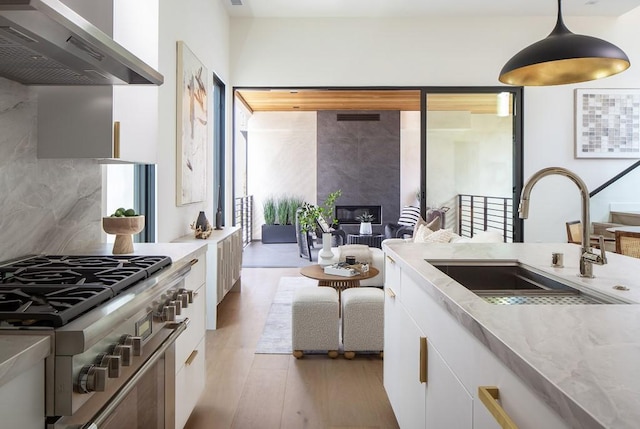 kitchen with decorative light fixtures, wall chimney exhaust hood, sink, and white cabinetry